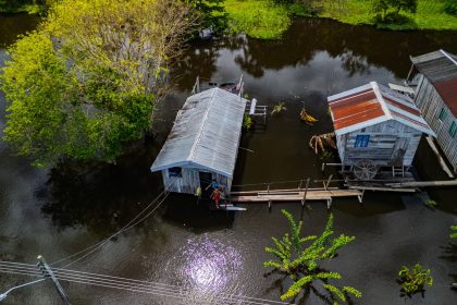 Vista aérea de casas ribeirinhas sobre área alagada, cercadas pelas águas e pela vegetação amazônica.