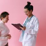 Médico de jaleco conversa com uma paciente sorridente em ambiente de atendimento.