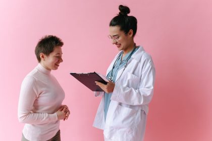 Médico de jaleco conversa com uma paciente sorridente em ambiente de atendimento.